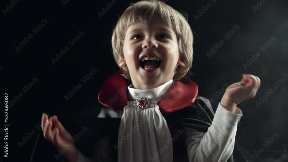 Happy little boy in vampire dracula costume smiling, rejoices sincerely on smoky colorful background. Halloween, trick or treat, party decoration concept. he will receive candies, treats Happy little boy in vampire dracula costume smiling, rejoices sincerely on smoky colorful background. Halloween, trick or treat, party decoration concept. he will receive candies, treats