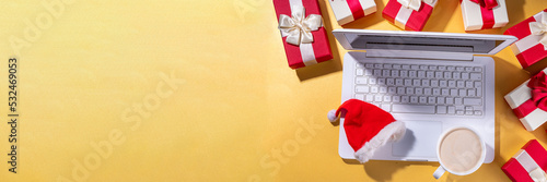 Christmas sale, preparation for holidays concept. Santa Claus hands with laptop, hot chocolate latte cup, gift boxes, flat lay on golden background. Making wishlist, preparation gifts for Christmas.