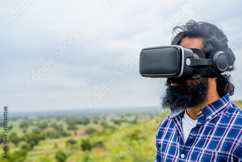 focus on VR, Young beard man using virtual reality headser on top of hill in rain with copy space - concept of technology, future and metaverse.