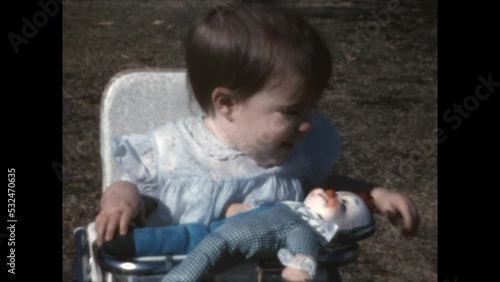 Baby and Doll 1965 - A child sits in a bouncy seat as her mother offers her a doll, in Canoga Park, California in 1965.  photo