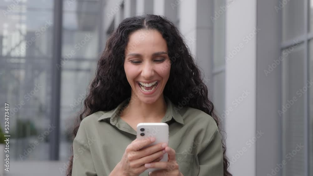 Hispanic Latin Caucasian 30s woman user blogger lady using mobile phone outdoors in city browsing receive offer SMS point with finger on smartphone wave head yes recommend online app good connection Hispanic Latin Caucasian 30s woman user blogger lady using mobile phone outdoors in city browsing receive offer SMS point with finger on smartphone wave head yes recommend online app good connection