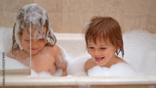 Adorable sisters - baby girls playing with Soap Foam in the bath. Fun and children hygiene concept