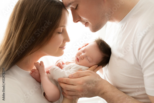 Close up portrait of young parents and newborn baby. Father and mother kiss and hug a beautiful newborn daughter. The concept of love, happy fatherhood and motherhood. Photography on white background.