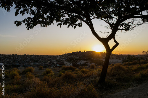 Lindo pôr do sol com silueta de árvore ao entardecer com céu dourado limpo, em pedreira no bairro Industrial, Contagem, Minas Gerais.