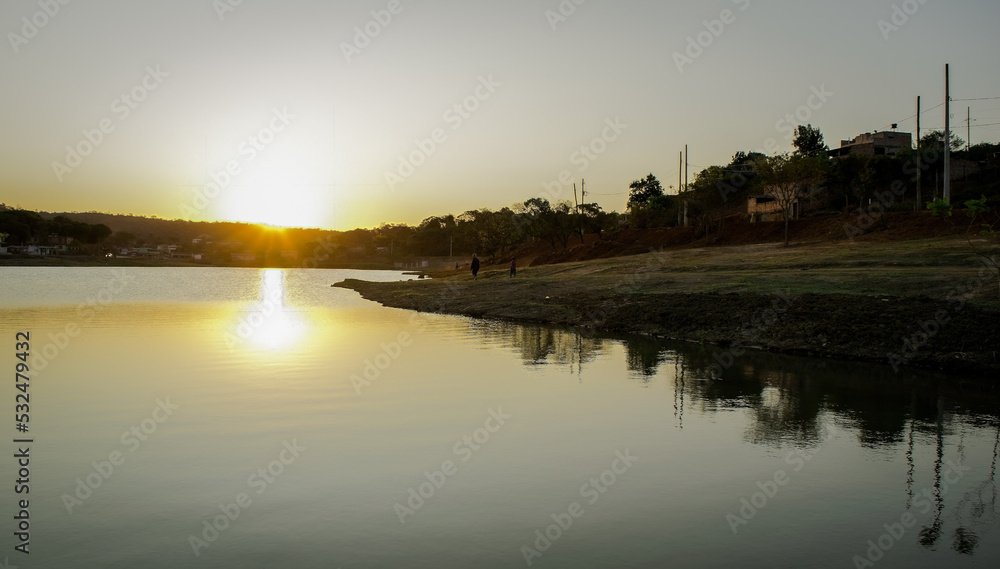 Pôr do sol ao entardecer com céu azul e limpo, com reflexo em lago no bairro Jardim das Oliveiras, Esmeraldas, Minas Gerais.