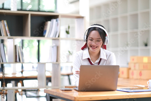 Young Asian woman student wearing headphones enjoy the convenience of using your laptop to study online at home interact with teachers effectively.