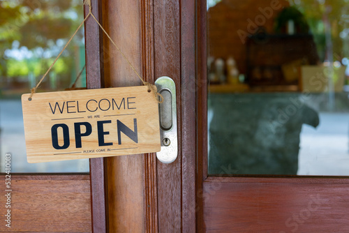 "Welcome and open" wording on wooden plate as sign in front of the entrance or door of coffee shop, restaurant, bar, pub and grocery store shows advertising message to customer for business.