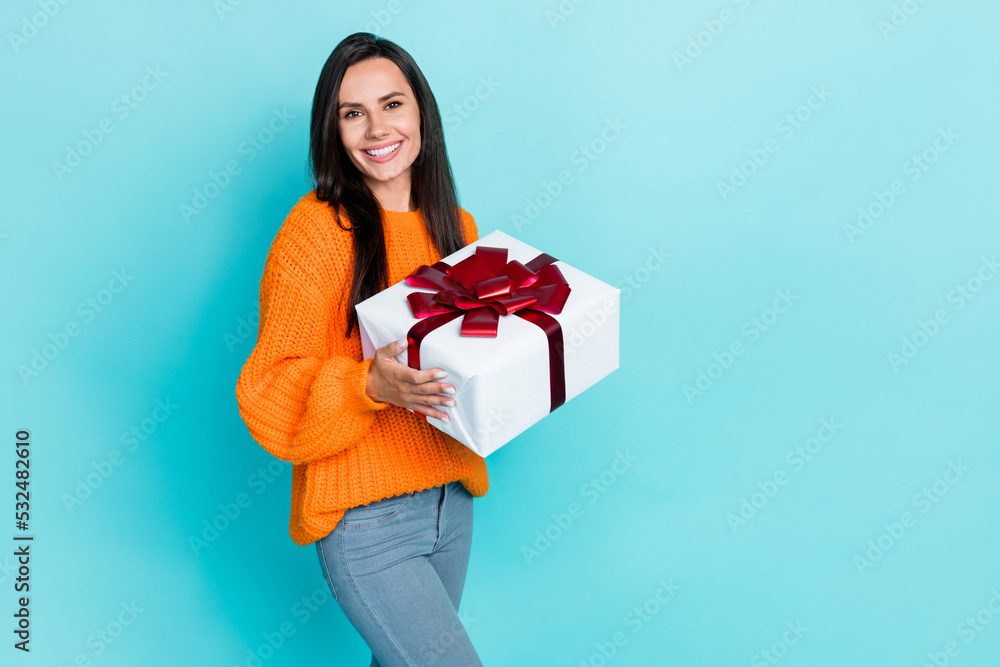 Photo of nice sweet girlish woman with straight hairstyle dressed orange jumper holding giftbox isolated on turquoise color background Photo of nice sweet girlish woman with straight hairstyle dressed orange jumper holding giftbox isolated on turquoise color background