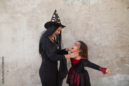 Happy halloween. Pretty young woman and girl dressed as witches on grey background play with terrifying and strangling gestures while having fun. Trick or treat. photo