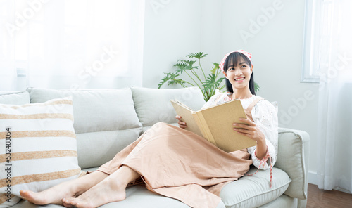 White cozy bed and asian beautiful girl, reading a book, concepts of home and comfort, place for text.Book worm love read book .Charming woman on cozy sofa interior.Vacation activity in home.