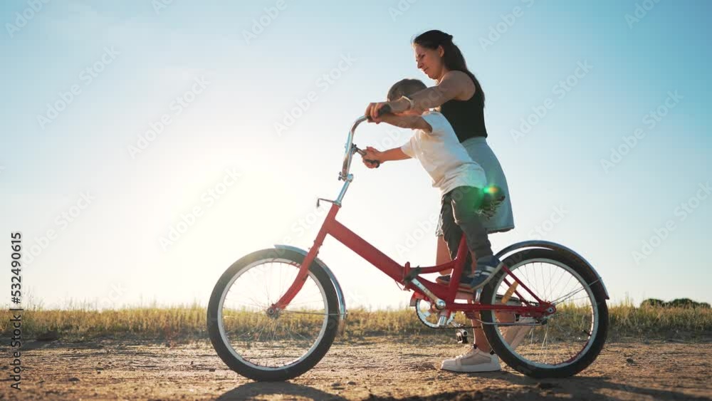 Happy family. Mom teaches her son to ride bike in park. My son is riding a bike for the first time. The child dreams of traveling by bike. The boy is learning to ride a bike. Mom helping hand to son. Happy family. Mom teaches her son to ride bike in park. My son is riding a bike for the first time. The child dreams of traveling by bike. The boy is learning to ride a bike. Mom helping hand to son.
