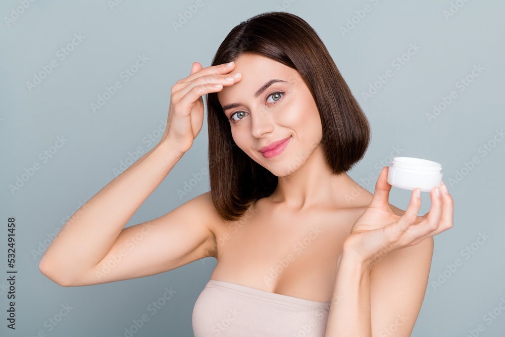 Photo of beautiful lovely girl applying anti wrinkles cream on forehead pampering isolated on grey color background Photo of beautiful lovely girl applying anti wrinkles cream on forehead pampering isolated on grey color background