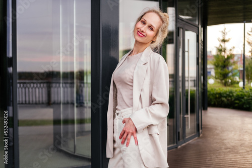 Smiling middle aged businesswoman in white clothes standing on street. Confident woman looking at camera outdoor Free Download Smiling middle aged businesswoman in white clothes standing on street. Confident woman looking at camera outdoor - GFXLoad