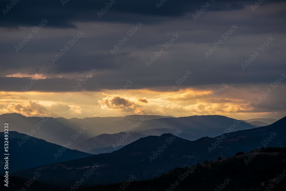 Panoramic view during sunset from Meteora rocks to Pindos mountains, the biggest mountain range of Greece, Thessaly district, Greece, Europe. Soft sun beam through clouds reaching the summit tops