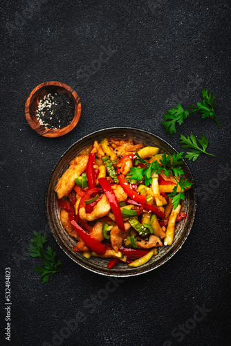 Asian cuisine, stir fry with chicken, red paprika pepper and zucchini bowl. Black kitchen table background, top view, copy space