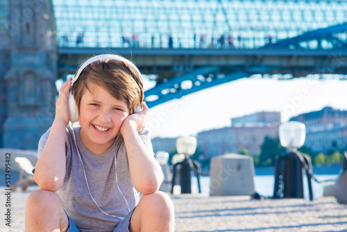 happy boy sits in the park, listens to his favorite music in headphones