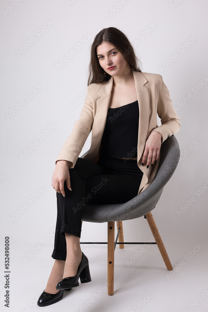 Portrait of a young brunette with long hair in the studio. Cute girl sitting on a chair on a white background. Portrait of a young brunette with long hair in the studio. Cute girl sitting on a chair on a white background.