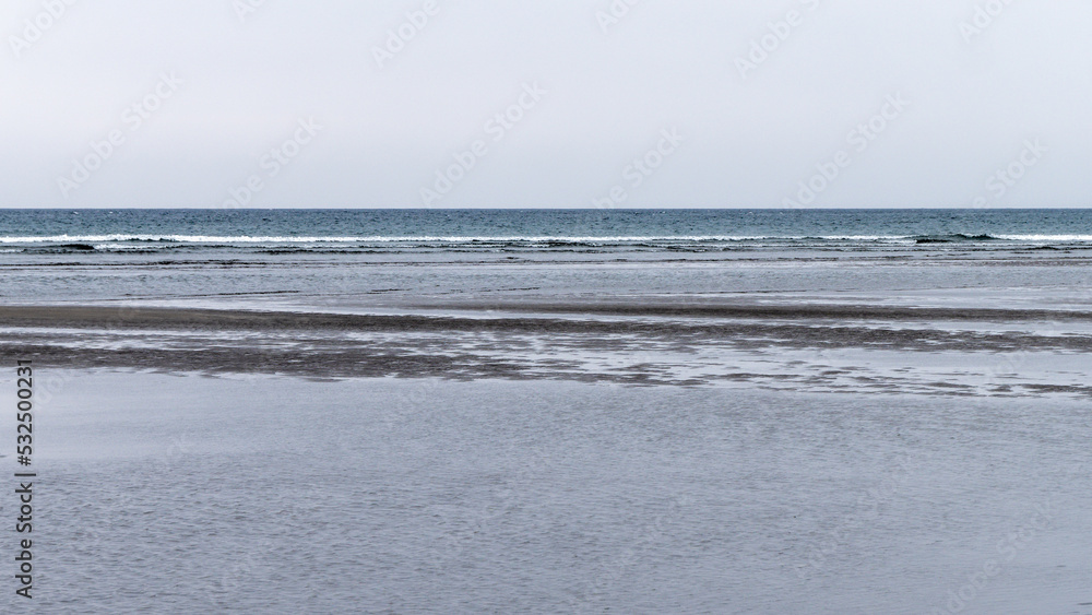 Obraz premium Wet sand. Gloomy seaside landscape. The harsh nature of the north of Europe. The cold coast of the Atlantic Ocean. Gray sand beach
