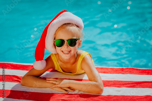 Girl with Christmas cap posing near the swimming pool on stripped towel.