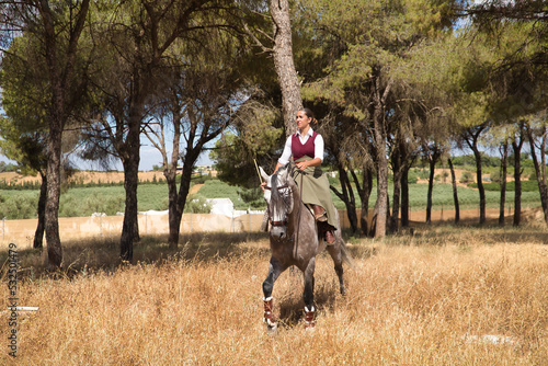 Woman horsewoman, young and beautiful, walking with her horse, through pine forest in the countryside. Concept horse riding, animals, dressage, horsewoman, cowgirl.