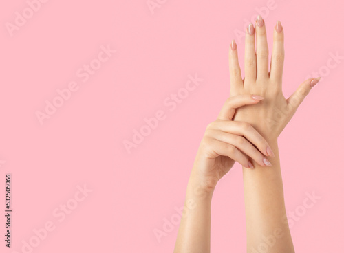 Hands of a beautiful well-groomed with feminine beige nude marble design nails gel polish on a pink background. Manicure, pedicure beauty salon concept.