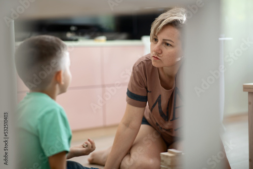 mom and son are playing a fun board game on laying wooden blocks in a tower and completing tasks while sitting on the floor at home having fun together