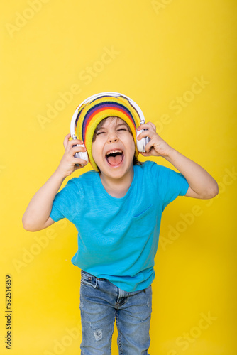 Handsome little boy in blue shirt and colorful hat with headphones, yellow background