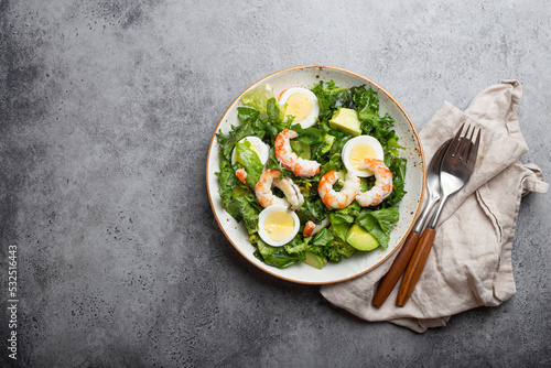 Healthy keto-friendly salad high in protein and healthy fats with shrimps, avocado and boiled eggs in ceramic boil on grey stone table background from above, diet clean eating concept. Copy space