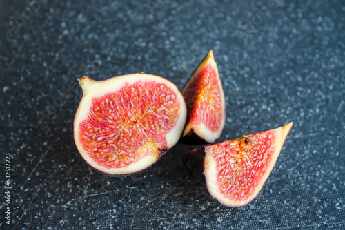 Close-up photo of a fig on a dark board. Ripe fruit whole and in pieces.