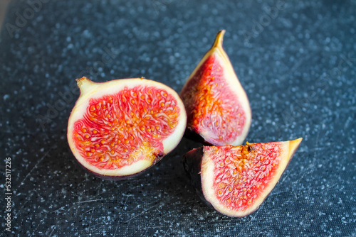 Close-up photo of a fig on a dark board. Ripe fruit whole and in pieces.