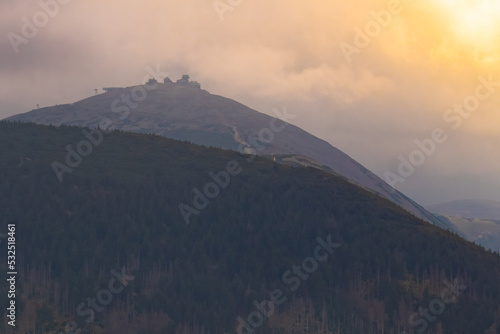 Photo of Śnieżka mountain in sunset sunligt in cloudy day. Karkonosze in Sudety Zachodnie Lower Silesia Voivodeship. Blue and orange colours shows beautiful view of landcape.