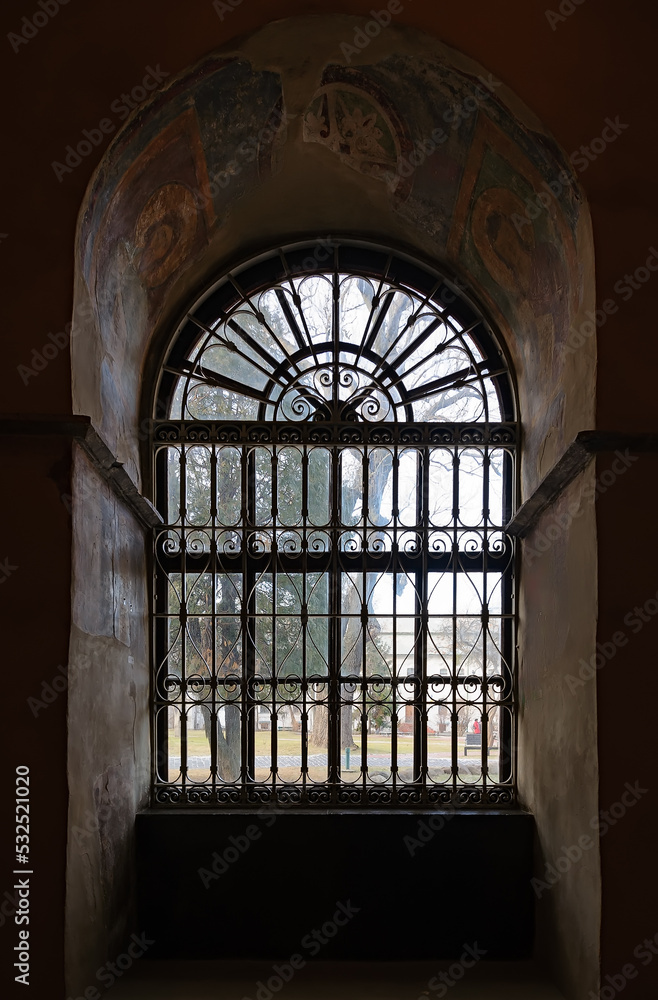 Old arched window in a church with iron grilles in front