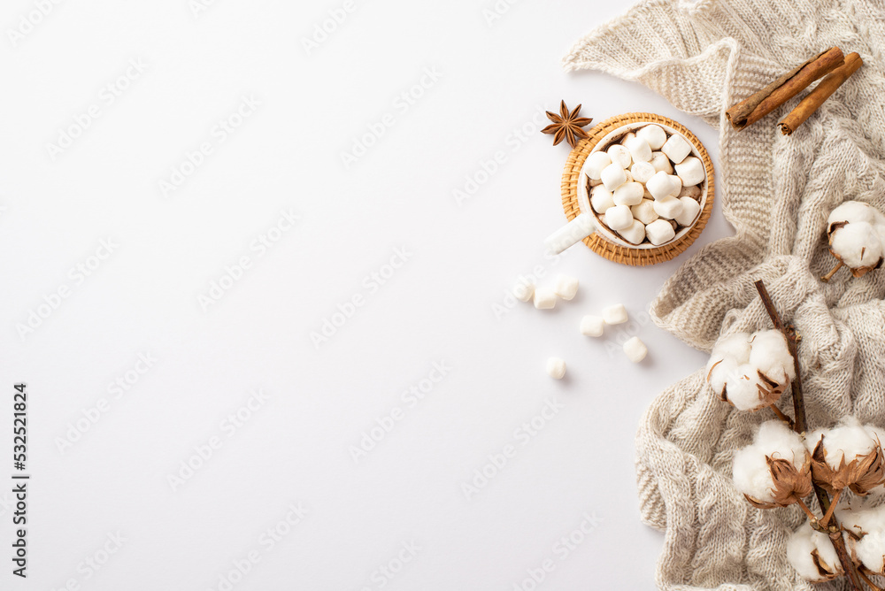 Fototapeta premium Winter mood concept. Top view photo of mug of hot drinking with marshmallow on rattan serving mat knitted scarf cotton branch anise and cinnamon sticks on isolated white background with empty space