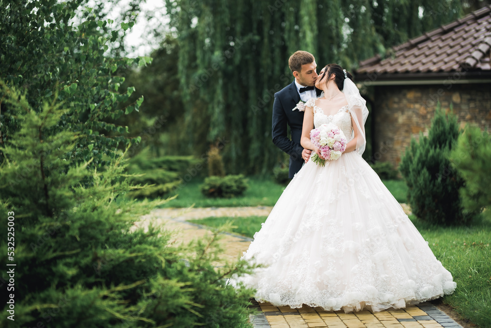 Beautiful bride and groom embracing and kissing on their wedding day outdoors Beautiful bride and groom embracing and kissing on their wedding day outdoors