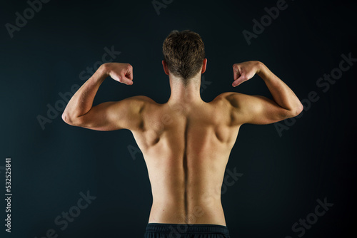 A man making muscles with his arms from behind showing a muscular and fit back on a black background