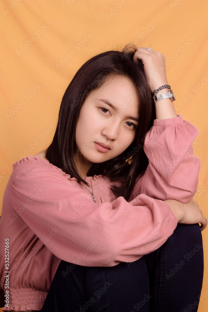 Naklejka premium Young Asian woman wearing a pink crop top. Stand up and take half the body on a yellow background. Express emotions.