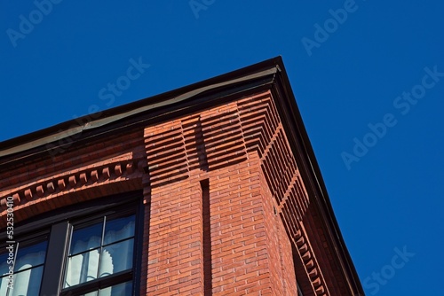 Decorative red brick cornice on 19th century textile mill building set against bright blue sky