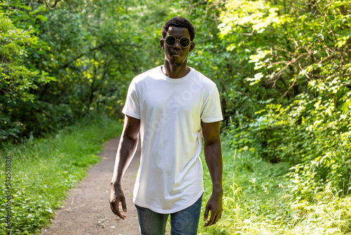 African american man in a white t-shirt walks in a green forest. Mock-up