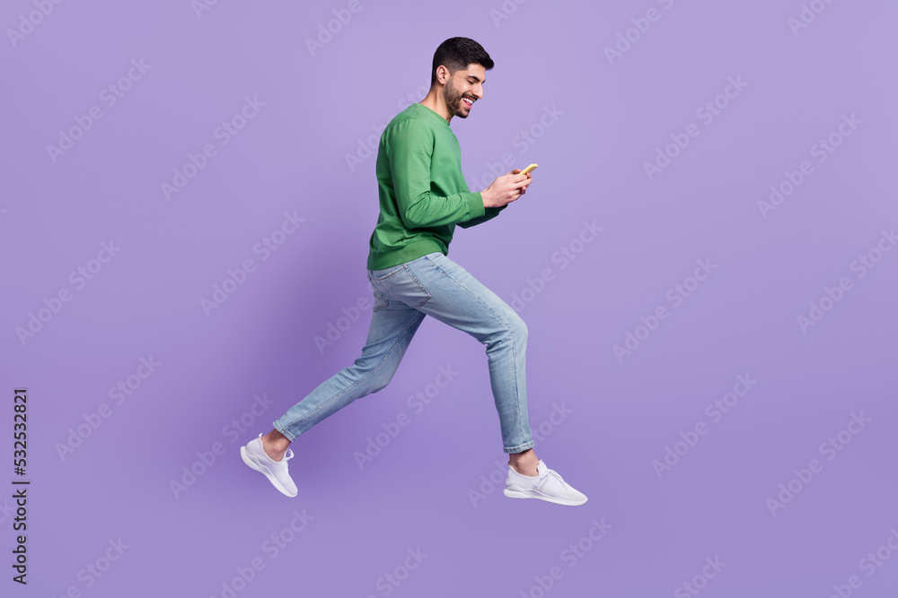 Full length photo of young handsome hispanic man hold gadget jump read news dressed trendy green look isolated on violet color background