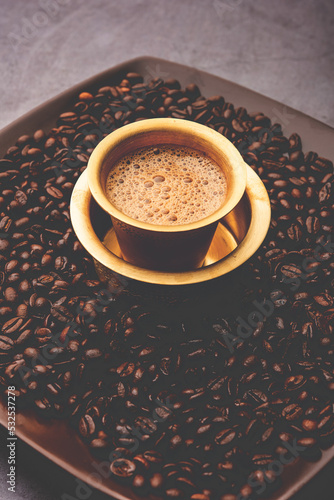 South Indian Filter coffee served in a traditional tumbler or cup over roasted raw beans photo