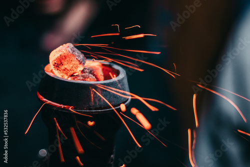 Hot red coals with hookah sparks in a metal bowl for hookah and traditional asian relaxation on a dark background