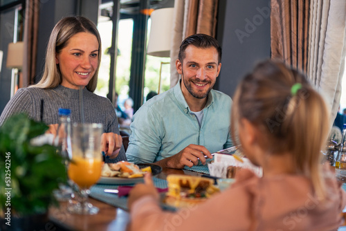 young married couple enjoys a fun lunch time with their little daughter in the restaurant.