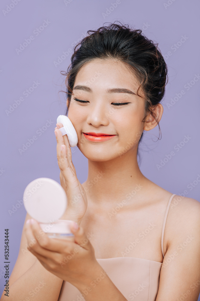 Beautiful Asian woman using powder puff to makeup