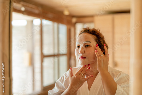 Woman skincare routine using facial mask in front of the mirror photo