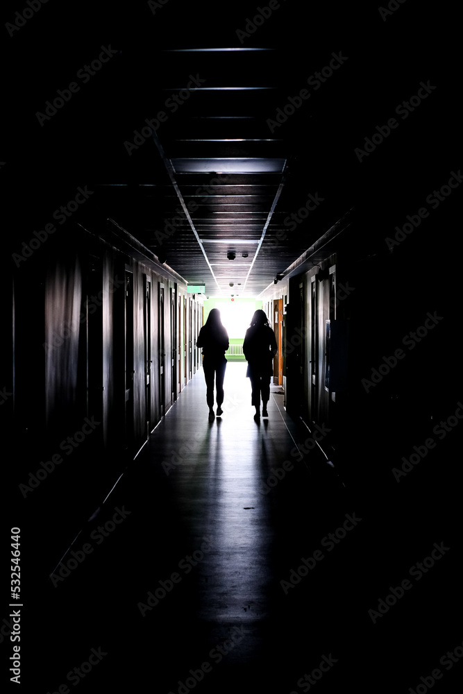 Two women walking alone in the dark. Two women, in a dark, long corridor, defocused