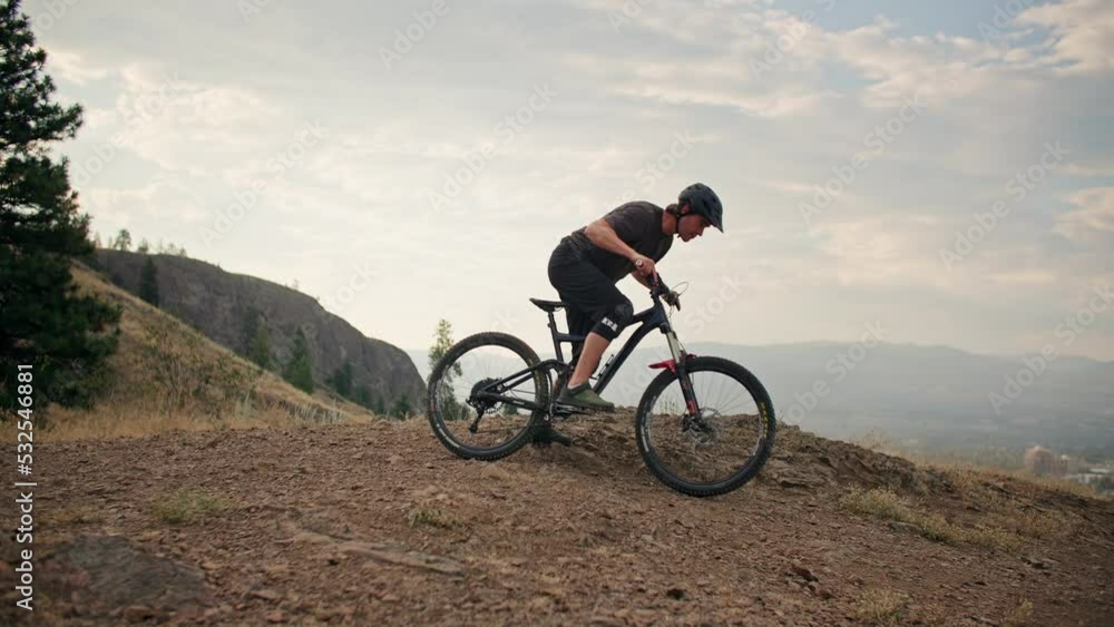 Wide of mountain biker getting on bike and riding in scenic mountain park Wide of mountain biker getting on bike and riding in scenic mountain park