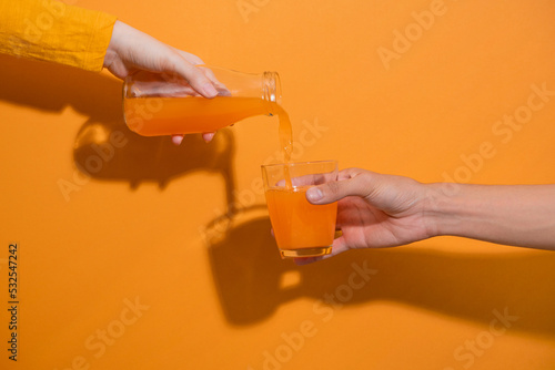 Hand pouring orange juice from jug with ice into glass photo