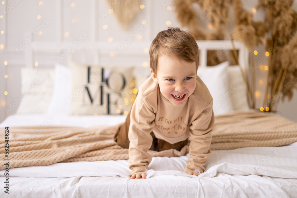 a small child on a bed in beige brown natural tones is laughing and rejoicing, a cheerful and funny little kid is playing at home a small child on a bed in beige brown natural tones is laughing and rejoicing, a cheerful and funny little kid is playing at home