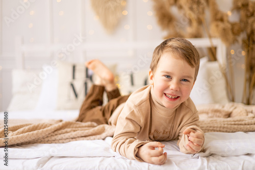 a small child on a bed in beige brown natural tones is laughing and rejoicing, a cheerful and funny little kid is playing at home