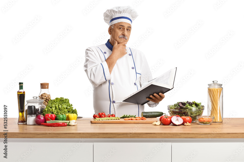Mature male chef behind a kitchen counter holding a cook book and thinking Mature male chef behind a kitchen counter holding a cook book and thinking